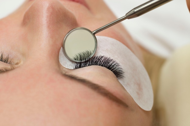 Photo eyelash extension procedure. beautiful woman with long eyelashes in a beauty salon. eyelashes close up. a mirror in the hands of a master