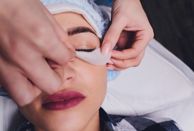 Eyelash Extension Procedure Close up view of female eye with long eyelashes Stylist holding pink tweezers tongs and making lengthening lashes Macro selective focus Beauty Concept Treatment