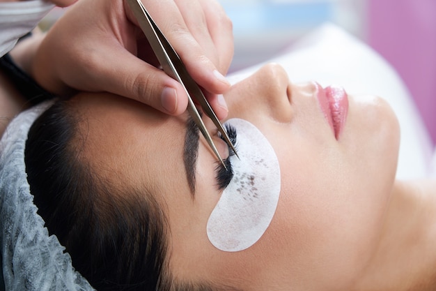 Eyelash extension procedure with tweezers in beauty salon