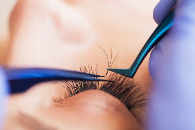 Eyelashes extensions. Fake Eyelashes. Eyelash Extension Procedure. Professional stylist lengthening female lashes. Master and a client in a beauty salon