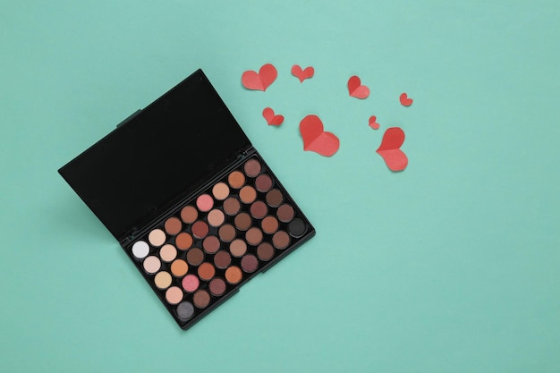 Eyeshadow makeup palette and hearts on blue background Beauty love glamour scene Top view
