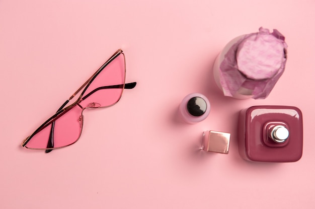 眼鏡、化粧品、香水。スタジオの壁にピンク色のモノクロのスタイリッシュでトレンディな構成。上面図、フラットレイ。周りのいつものものの純粋な美しさ。広告のコピースペース。ファッション。