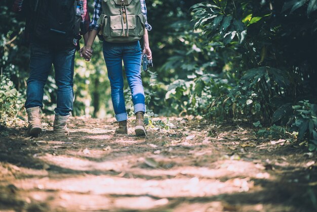 f benen van jonge actieve reizigers houden handen tijdens het wandelen in het bos