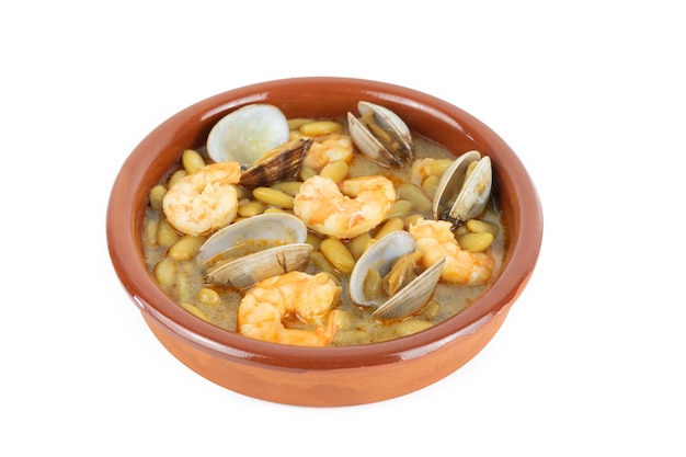 Fabas verdinas with prawns and clams in an earthenware casserole on a white background. Copy space.