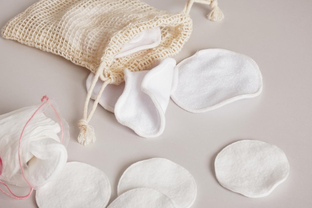 Fabric and cotton pads for cleansing the skin from make-up, a mesh bag and a plastic bag for storing them on a beige background Zero waste, reusable, eco, makeup remover and washing concept.