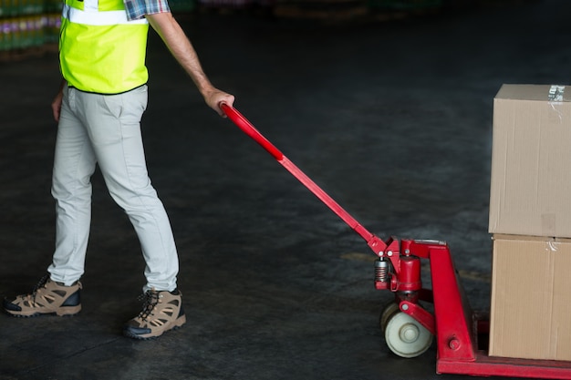 Fabrieksarbeider die karretje van kartondozen trekt