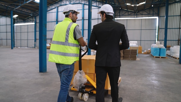 Fabrieksarbeiders leveren dozenpakket op een duwende trolley in het magazijn. Industrie supply chain management concept.