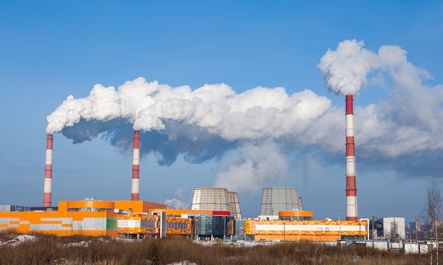 Fabriekshoofdleidingen die veel rook in de atmosfeer uitstoten. De blauwe lucht wordt verduisterd door rook uit fabrieksschoorstenen