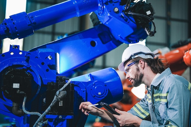 Foto fabrieksingenieur inspecteert op machine met slimme tablet werknemer werkt aan robotarm van zware machine de lasmachine met een systeem op afstand in een industriële fabriek kunstmatige intelligentie concept