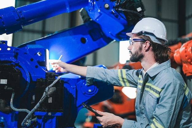 Fabrieksingenieur inspecteert op machine met slimme tablet Werknemer werkt aan robotarm van zware machine De lasmachine met een systeem op afstand in een industriële fabriek Kunstmatige intelligentie concept