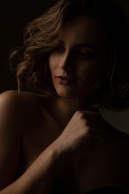 Fabulous brunette woman with curly hair wears lingerie posing with contrast light at studio