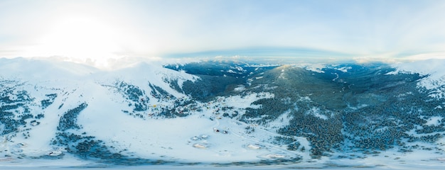 Fabulous evening panorama with snow-capped mountains and hills with bright sun and fog on a frosty winter evening. Beautiful harsh northern nature concept. Copyspace