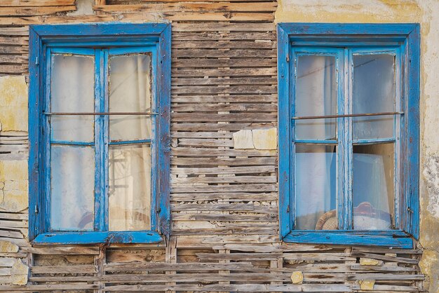 Facade of a crumbling old wooden house with blue windows Abandoned houses of the old city idea for background