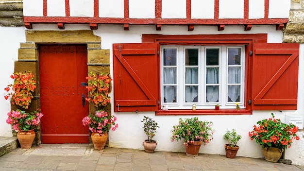 Facade of a fairytale house with potted plants and red and white colors. France