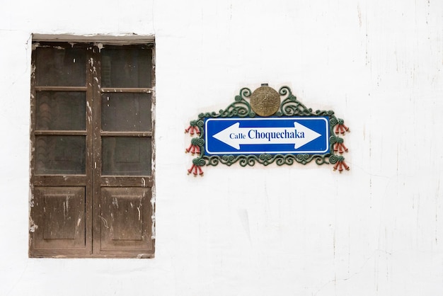 Facade of a house in Cusco where you can see a wooden window and a sign with a street sign