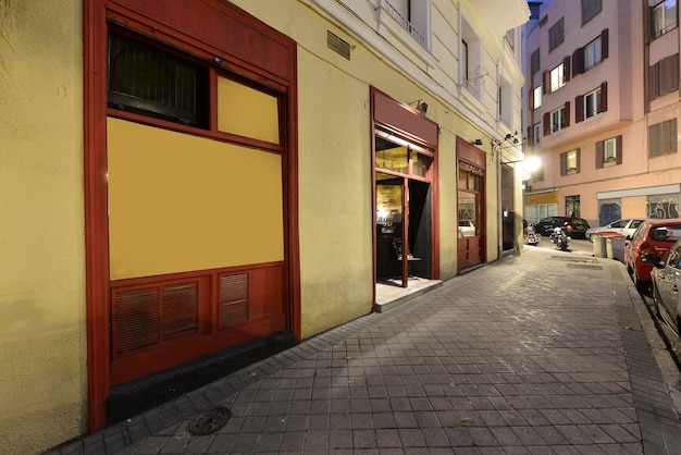 Фасад местного бара с желтым фасадом и металлическими окнами, окрашенными в красный цвет