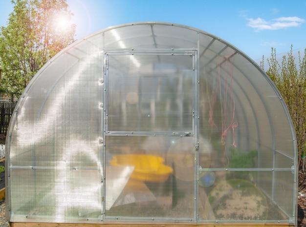 Facade of a modern polycarbonate greenhouse on a private plot against a blue sky spring outdoors