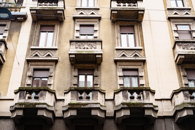 Facade of an old house with carved stone balconies and shutters on the windows milan italy