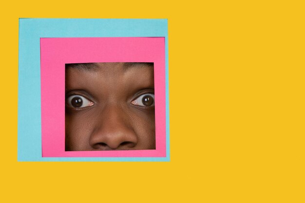 Face of african-american man peeking throught square in yellow background