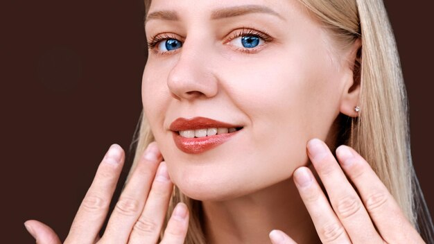 Face of beautiful smiling woman with natural makeup looking at camera closeup young girl touches her