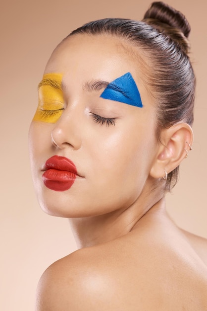 Face beauty and makeup with shapes on a woman in studio on a beige background to promote or model cosmetics Wellness cosmetics and art with an attractive young woman posing for creative skincare