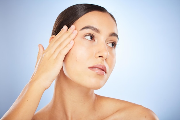 Face beauty and skincare with model woman in studio on a blue background thinking about natural treatment Makeup wellness and aesthetic with an attractive young female posing to promote a product