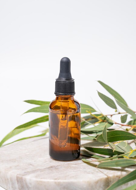 Face and body serum in bottle on a marble board on a white background with green leaves