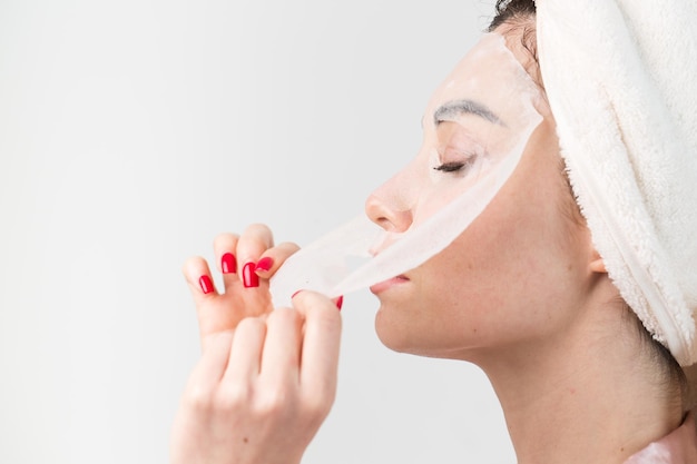 Face care and beauty treatments Woman with a sheet moisturizing mask on her face isolated on white background