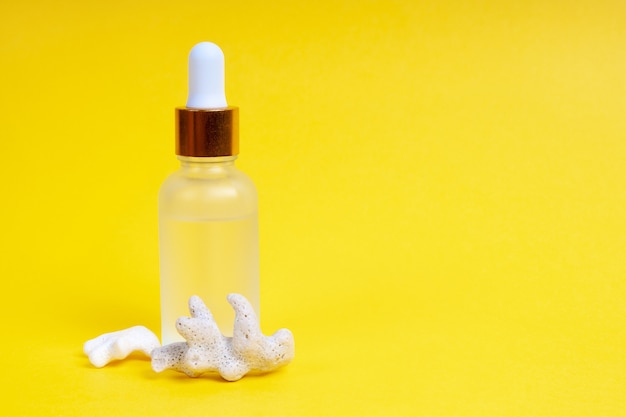 Face care in a glass dropper bottle with sea coral on a yellow background. Skin care concept.