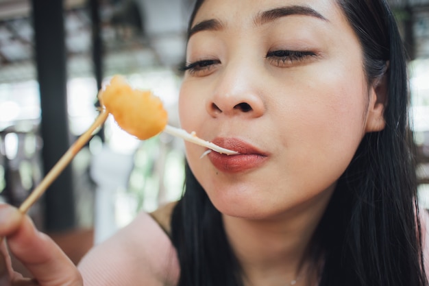 女性の顔のクローズアップは棒でチーズボールを食べる。