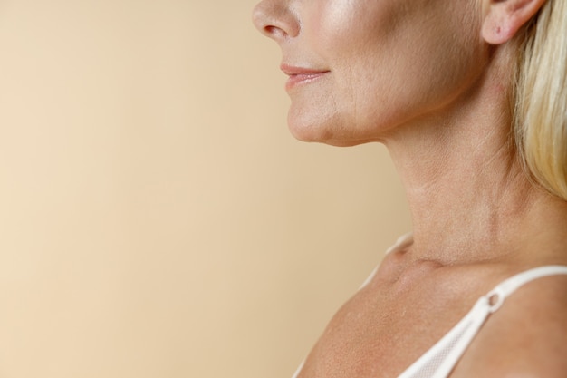 Face closeup of mature blonde woman in white underwear smiling away standing isolated over beige