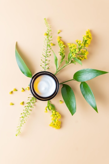 Face cream moisturiser glass jar on beige background with yellow spring flowers skincare and cosmetic beauty product concept