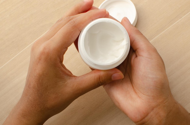 Face cream for the skin Person using white cream in white bottle for body care Hands about to apply.