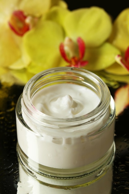 Face cream with orchid flowers on dark background