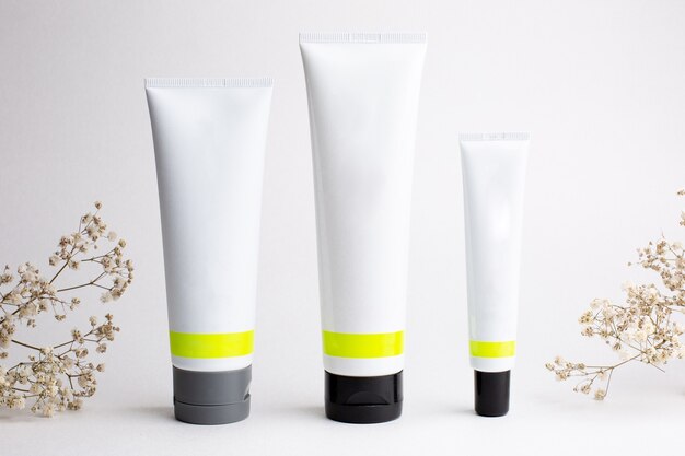 Face creams in plastic packagings on a white background with flowers