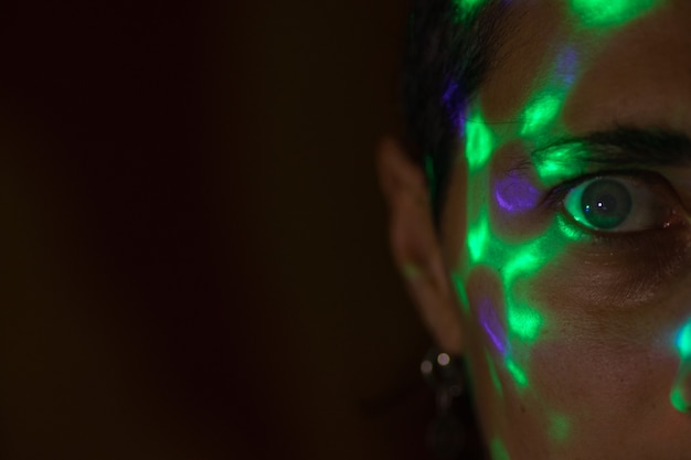 a face in the dark covered with bright colored spots from a bright lamp colored glare from the lamp