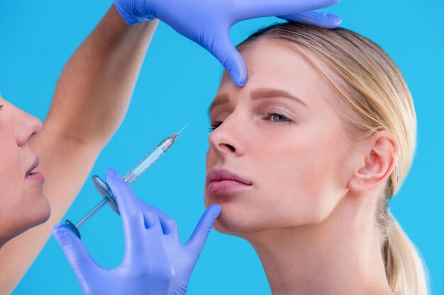 Face of a girl with smooth skin without wrinkles makes beauty shots syringe next to the face skin care salon gloved hands closeup portrait skin care beauty concept surgery youth