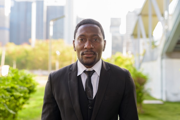 Face of handsome bearded African businessman in suit at the park