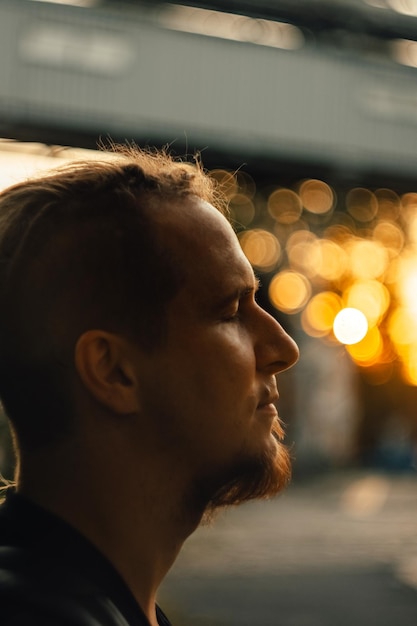 The face of a handsome man with a beard in profile at sunset with golden bokeh like a cinematic