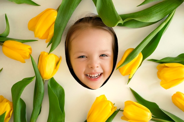 Face of a happy laughing child surrounded by yellow tulip flowers Hello spring