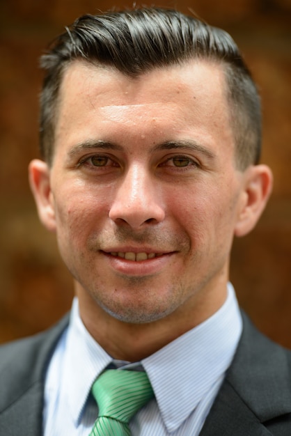 Face of happy young businessman in suit smiling against brick wall