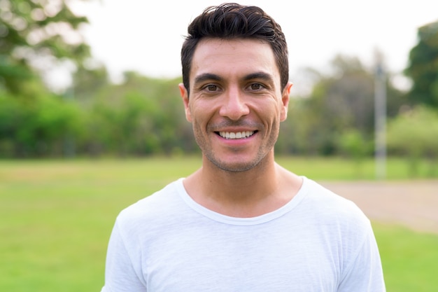 Face of happy young handsome Hispanic man smiling at the park