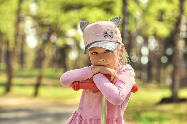 Foto il volto di una bambina con un berretto che tiene le maniglie di uno scooter