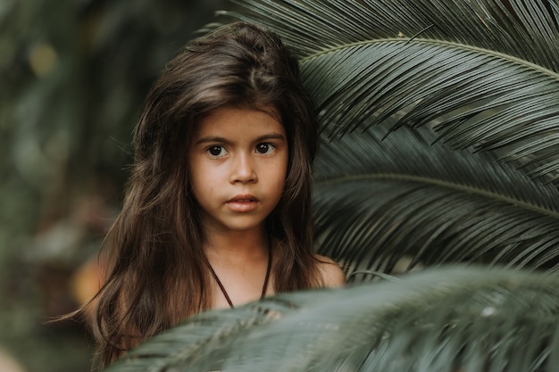 face of a little girl surrounded by tropical leaves Closeup portrait of a beautiful swarthy baby