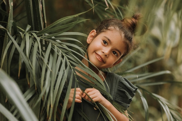 face of little girl surrounded by tropical leaves Closeup portrait of swarthy kid with perfect skin