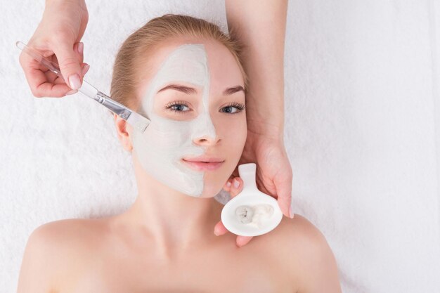 Face mask apply, spa beauty treatment, skincare. Woman getting facial care by beautician at spa salon, top view