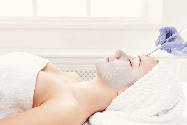 Face mask, spa beauty treatment, skincare. Woman getting facial nourishing mask by beautician at spa salon, side view, closeup