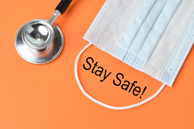Face mask and stethoscope over orange background written with STAY SAFE