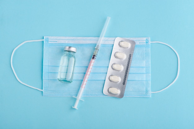 face mask and syringe and blister of pills on blue background