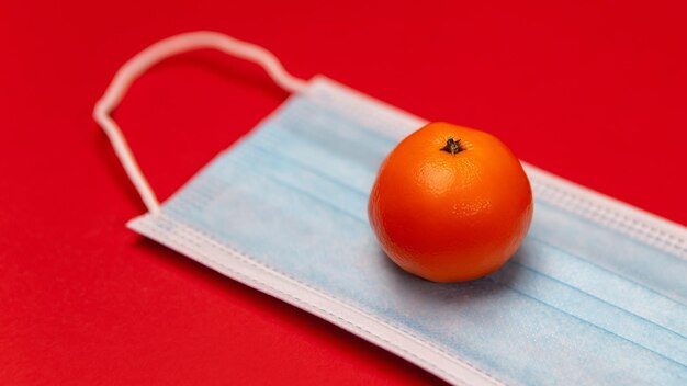 Face mask and tangerine on red background